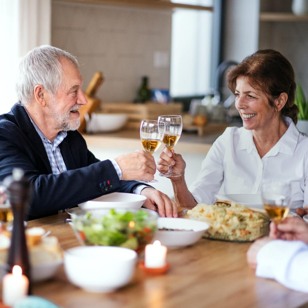 Older couple clinking wine glasses, enjoying meal together, smiling