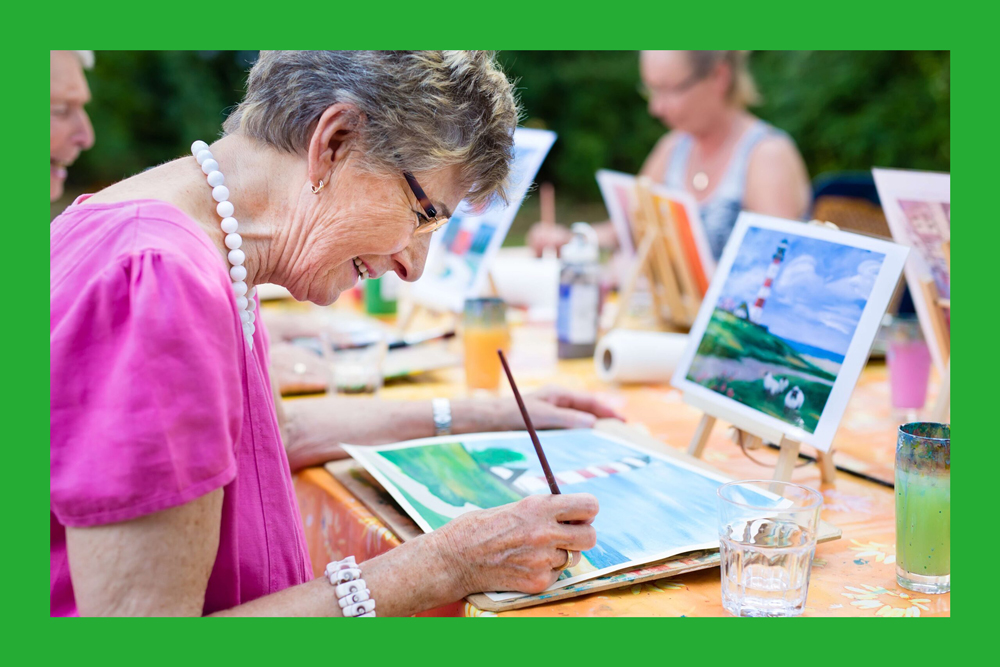 Older woman painting in group, outdoors