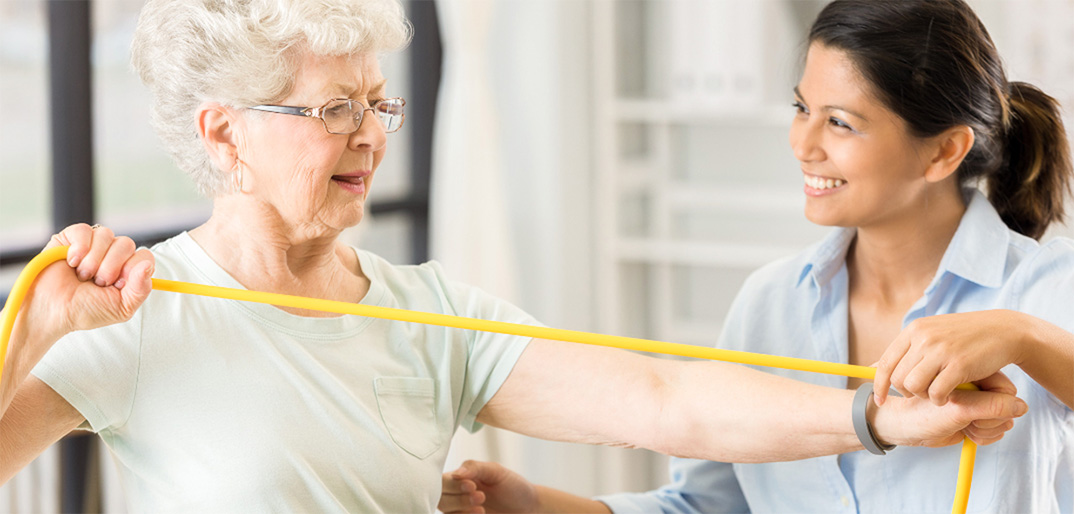 Older woman using resistance band, working with female caregiver, orthopedic rehabilitation