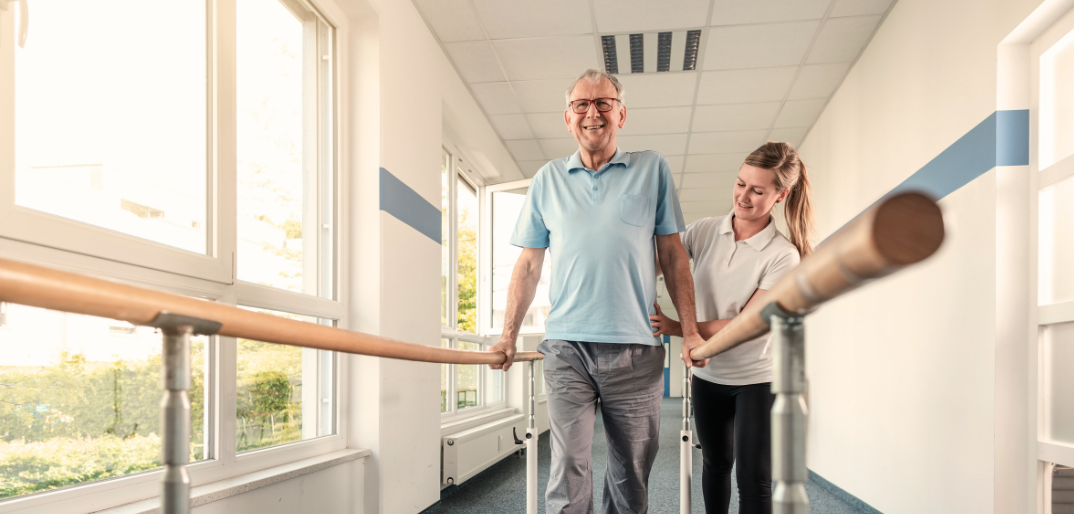 Stroke recovery, older male holding himself up on parallel bars with female physical therapist,